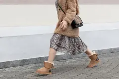 Woman striding in street wearing artificial fur coat, long dress leopard print and UGG style comfort boots