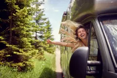 Happy lady hanging out window of RV with breeze in hair