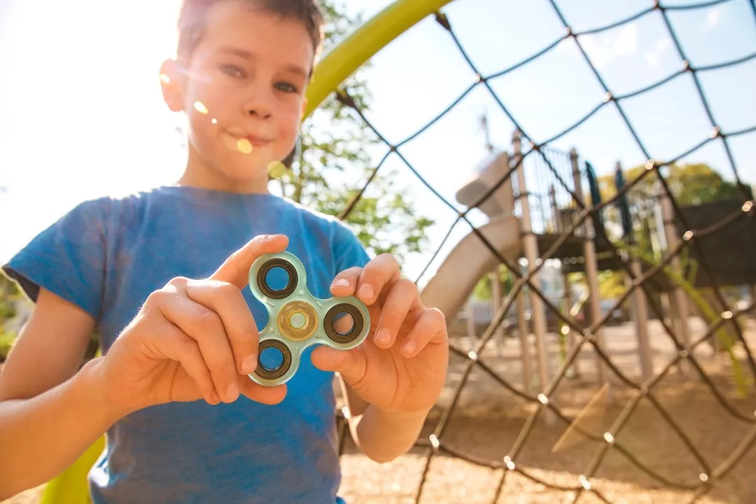 boy holds a spinner fidget in his hands. satisfied kid plays with a spinner on the playground. Blurred background.