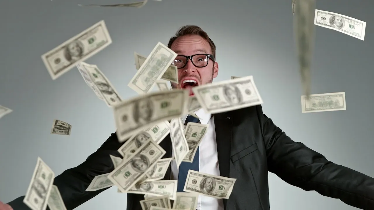 Dollar bills falling from the sky in front of man with wide-eyed open mouthed expression