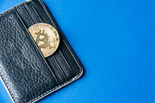 Black leather wallet on a blue background with several gold and silver coins of bitcoins falling out of their pockets.