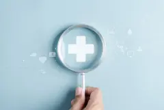 Magnifying glass over white cross depicting zooming in on healthcare sector