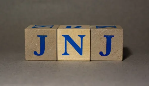 Stock Ticker symbol of Johnson & Johnson JNJ, made of wooden cubes, on a gray background.