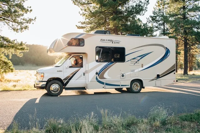 Thor Industries Freedom Elite RV driving on road in sunlight with trees and water behind