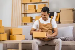 Men working from home, managing an online small business, sitting on the sofa, checking items, packing products, and preparing orders for shipment