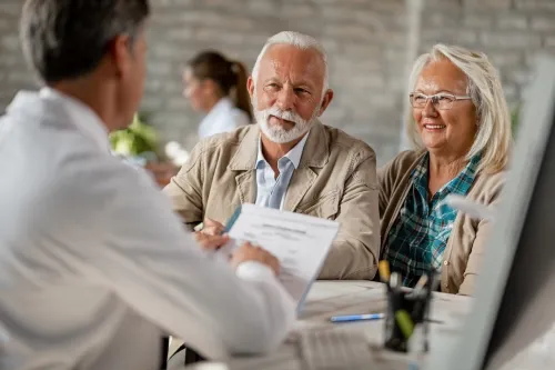 Happy senior couple going through medical insurance paperwork with a doctor.