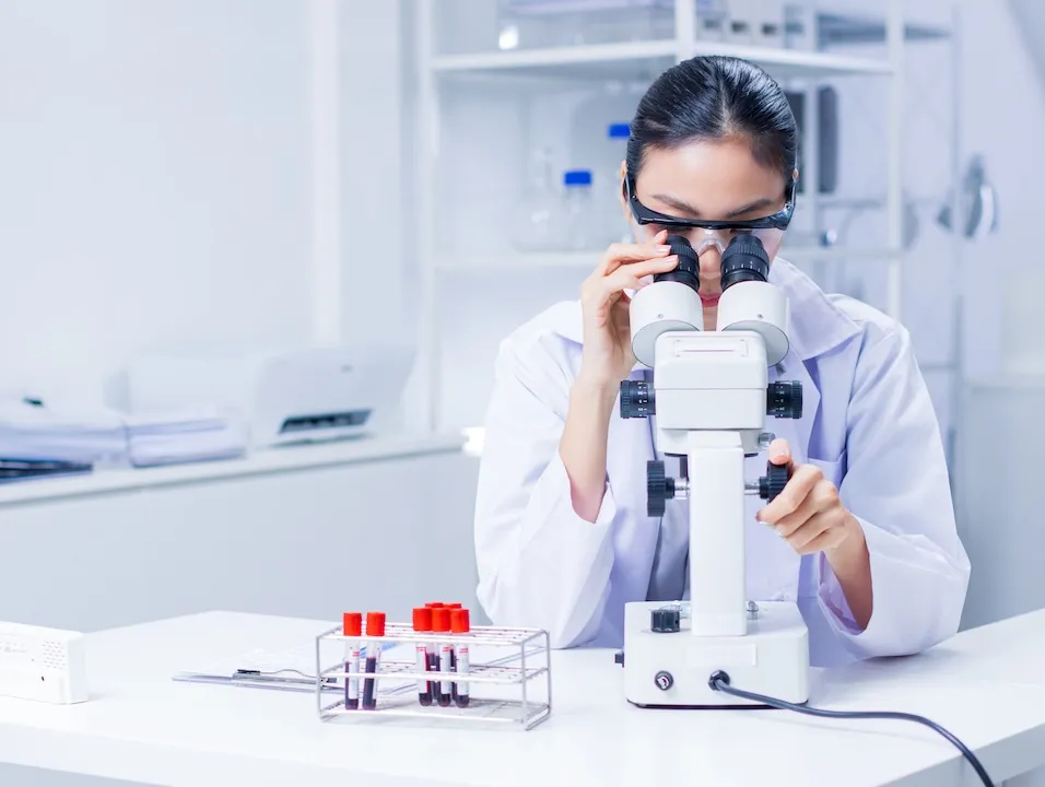 Professional asian female scientist works in laboratory using microscope examining chemical samples conducting experiments and analyzing samples advancing studies in vaccine development.