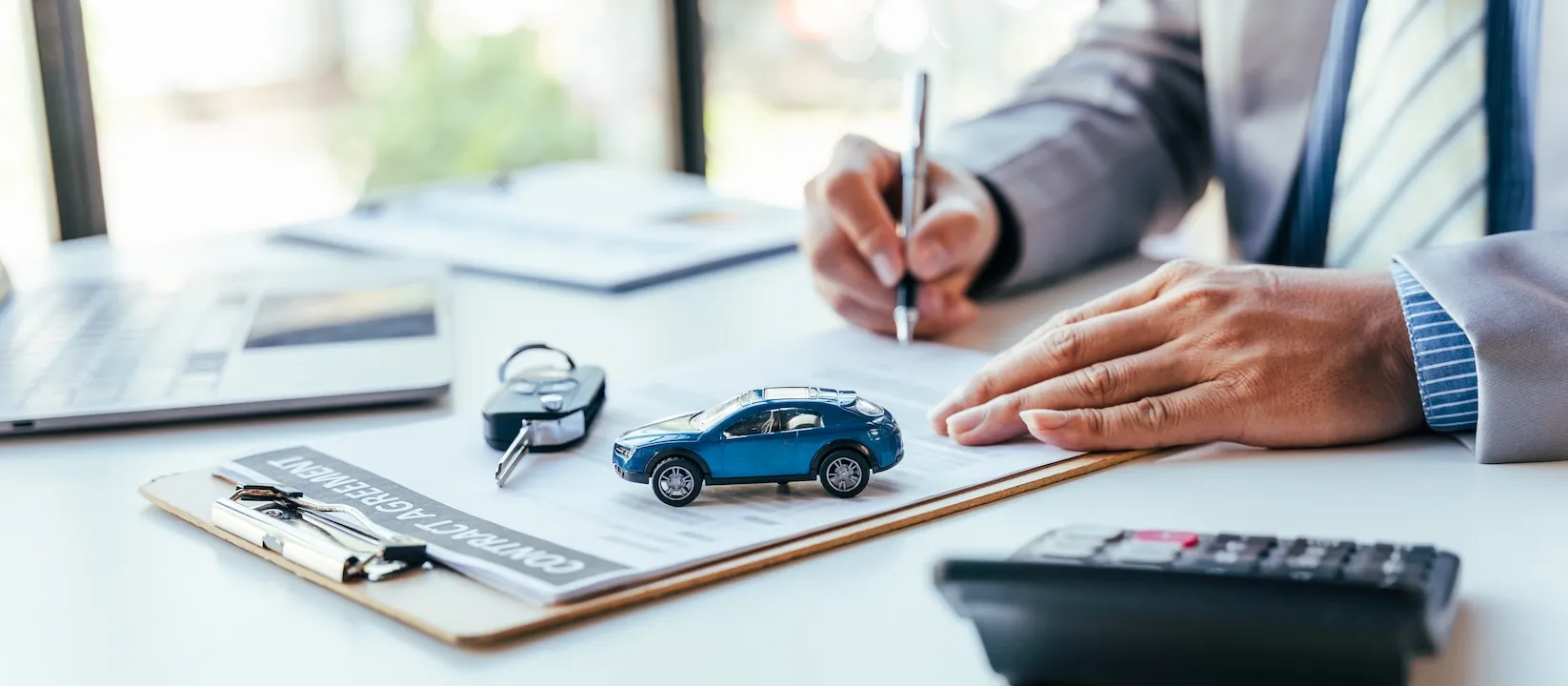 Man signing car insurance document or lease paper. Writing signature on contract or agreement. Buying or selling new or used vehicle. Car keys on table.