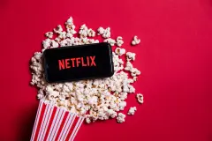 Netflix Logo on smartphone sitting in pool of popcorn pouring out of popcorn bucket