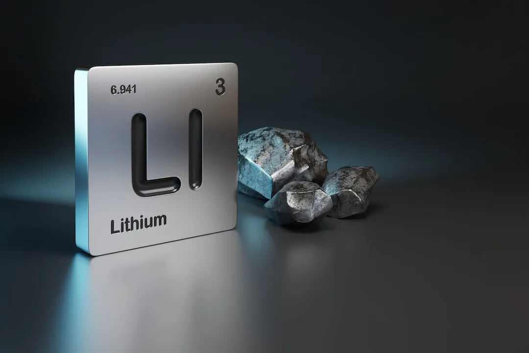 LI Lithium etched on Silver Tile next to silvery rocks