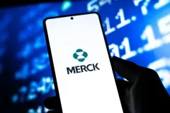 Merck Logo on Smartphone with stock trading screen behind