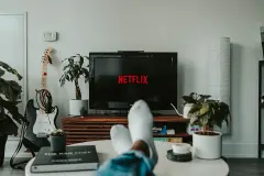 A Person watching Netflix on TV with their feet up on the table in front of them.