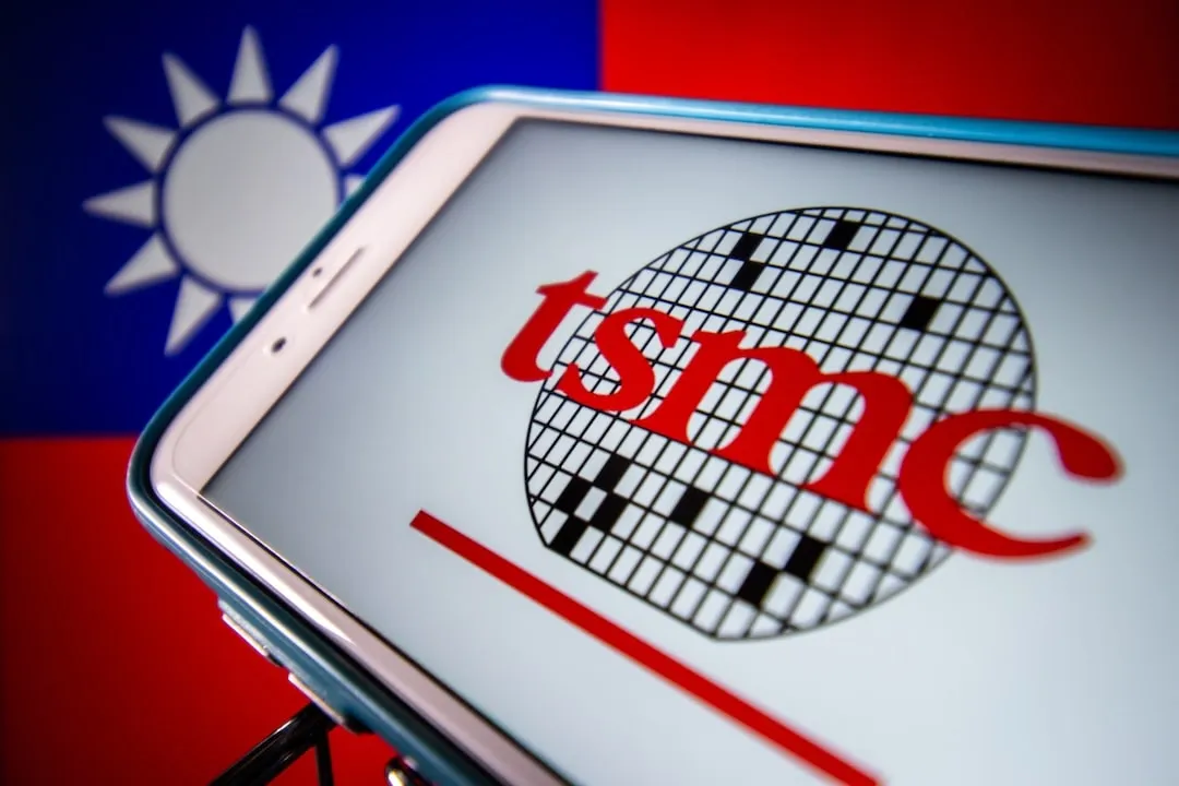 The image displays a smartphone with the logo of Taiwan Semiconductor Manufacturing Company (TSMC) on its screen, with the flag of Taiwan in the background.