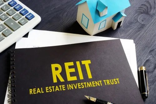 REIT Real Estate Investment Trust in Yellow on black ringbound notepad next to calculator