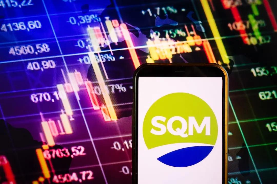 SQM Logo on smartphone against stock trading screen background.
