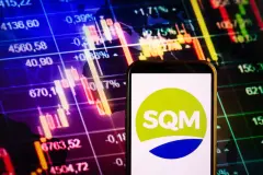 SQM Logo on smartphone against stock trading screen background.