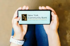 New York Community Bank Logo on smartphone being held in two hands.