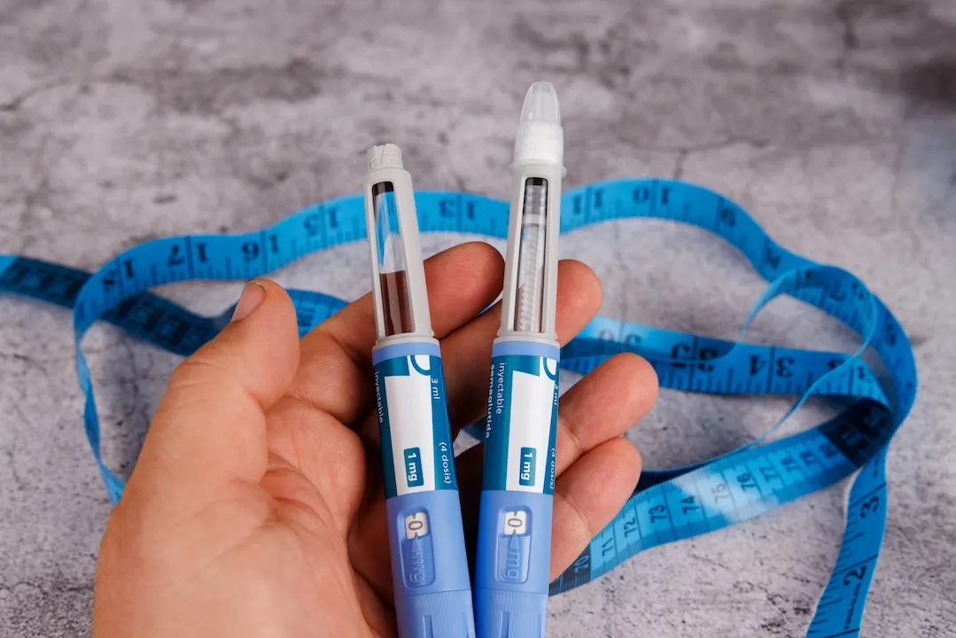 Hand with semaglutide pens and measuring tape on cement surface