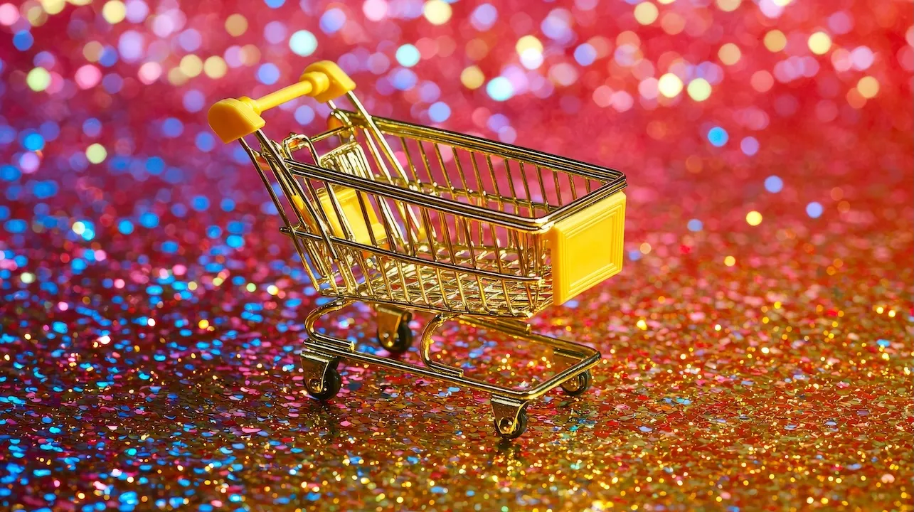 A small shopping cart stands on a glittery surface under bold red lights, creating a lively and eye-catching scene full of color and dynamic energy.