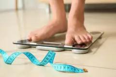 Tape in front of woman standing on floor scales indoors. Overweight problem