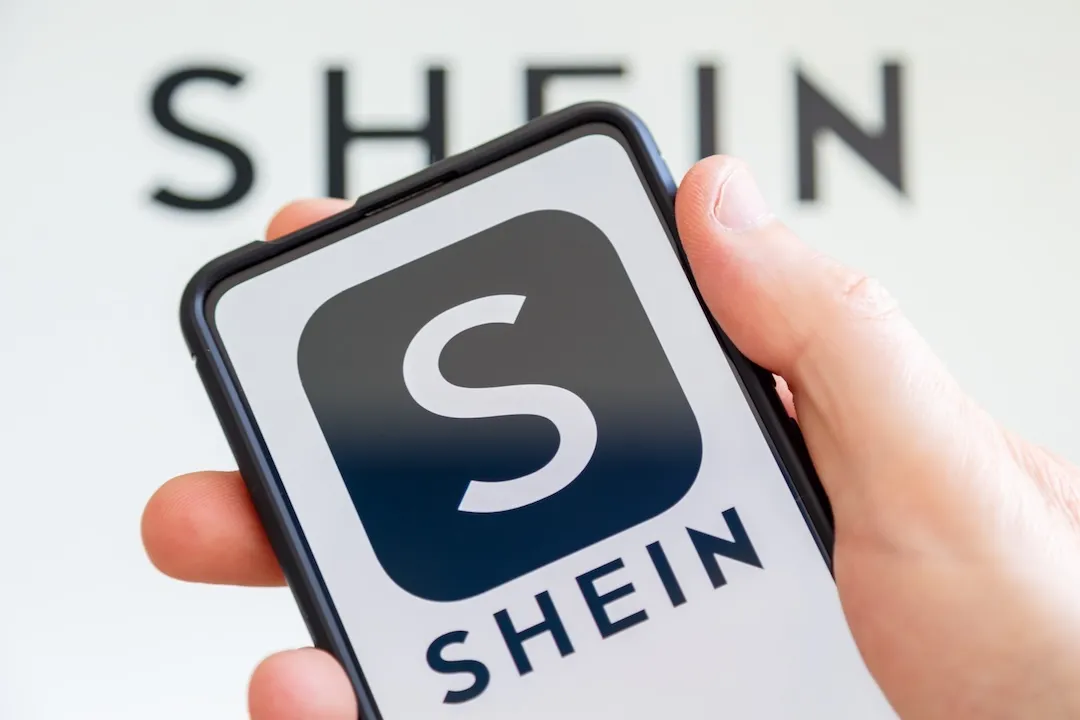 Hand holding a mobile phone with Shein logo online marketplace ecommerce computer screen