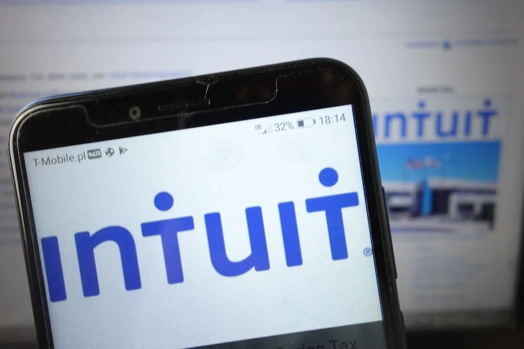 Intuit Logo on smartphone screen with Intuit website on screen in background.