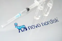 Vials of liquid on a white table and the logo of a large pharmaceutical company.