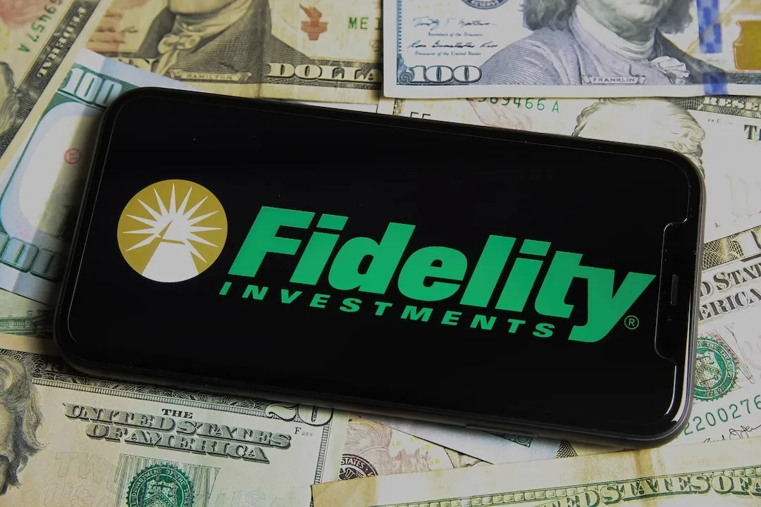 Fidelity Investments. Closeup of mobile phone with logo of fidelity investments, us dollar paper banknotes background