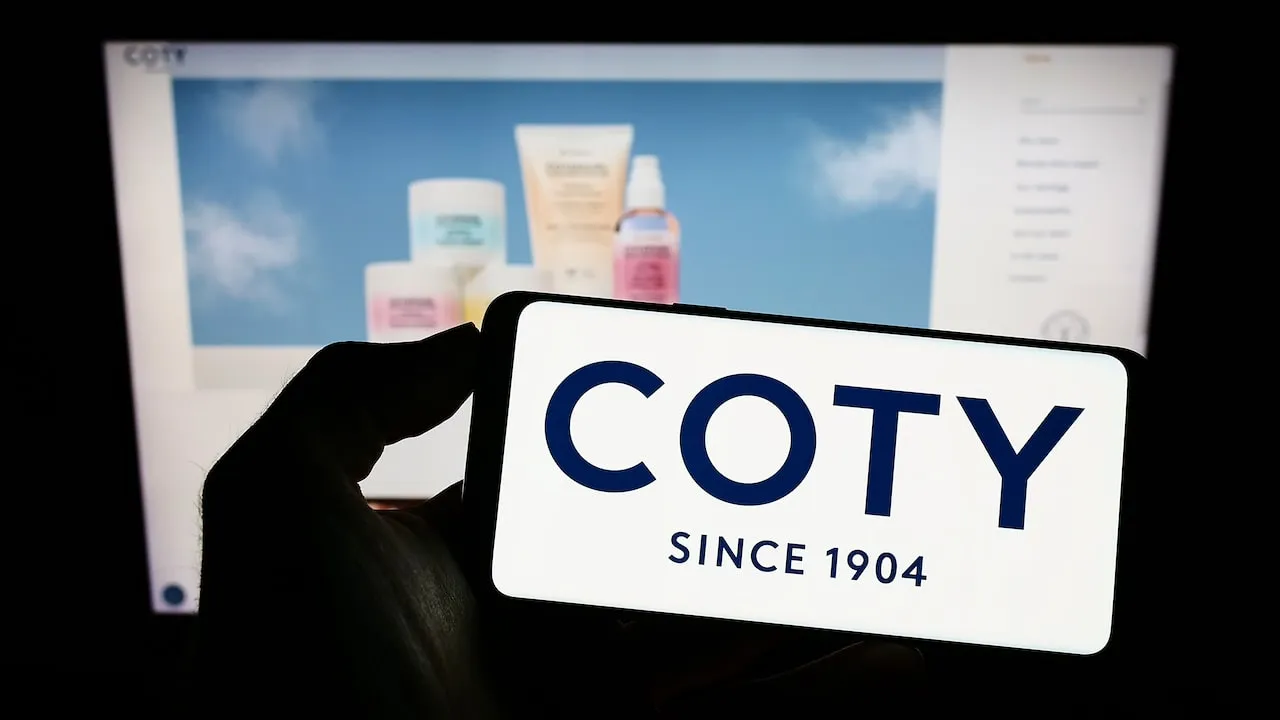 COTY Logo on smartphone screen with Coty cosmetics in background.