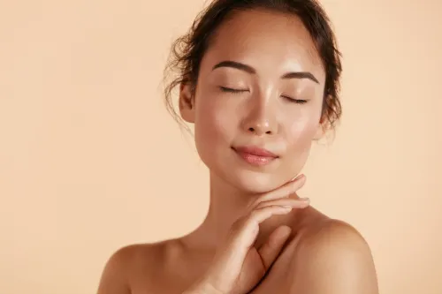 Beauty face. Woman with natural makeup and healthy skin portrait. Beautiful asian girl model touching fresh glowing hydrated facial skin on beige background closeup. Skin care concept See Less