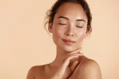 Beauty face. Woman with natural makeup and healthy skin portrait. Beautiful asian girl model touching fresh glowing hydrated facial skin on beige background closeup. Skin care concept See Less