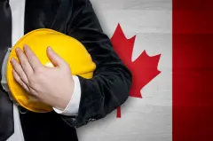 Man holding yellow hardhat in front of Canadian Flag.