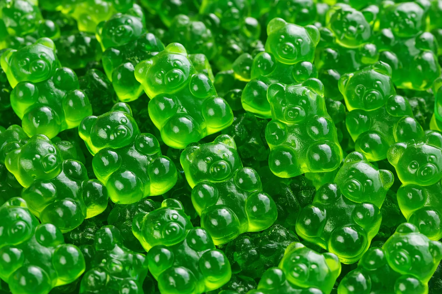 Translucent green gummy bears clustered together with glossy texture