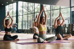 Group of young people practicing yoga In the prayer position and raised hands while sitting on mat at gym.