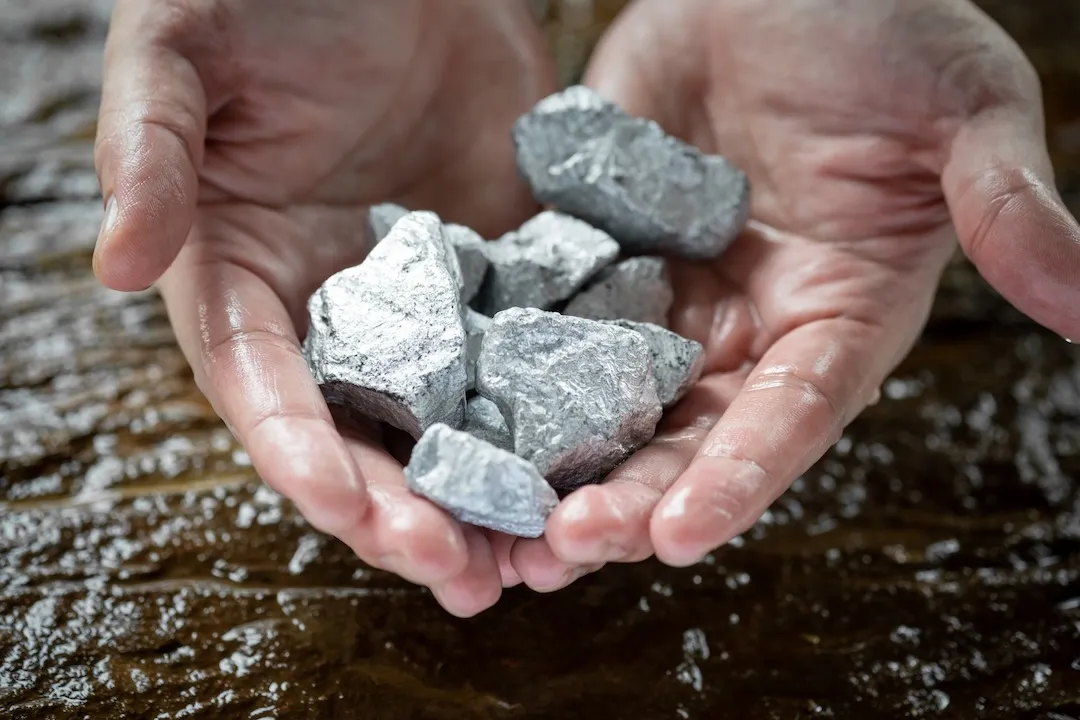 Miners hold in their hands silvery white rare earth minerals found in the mine for inspection and consideration