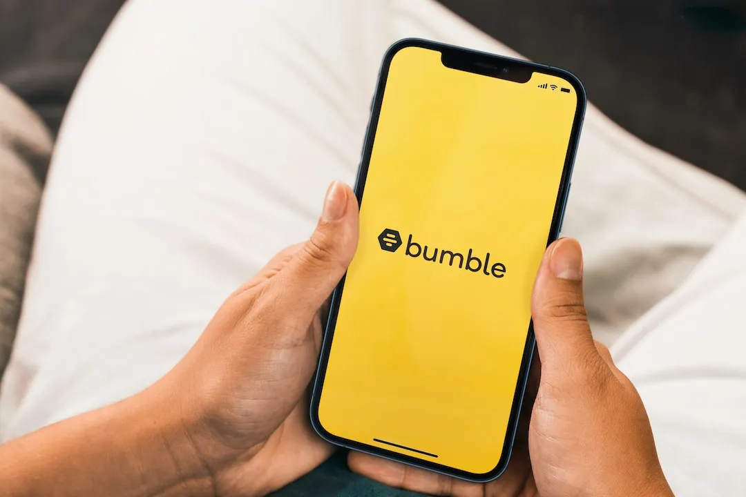 black Bumble logo on yellow background on Smartphone screen held in two hands.