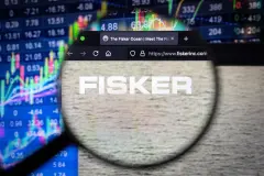 Fisker company logo on a website with blurry stock market developments in the background, seen on a computer screen through a magnifying glass