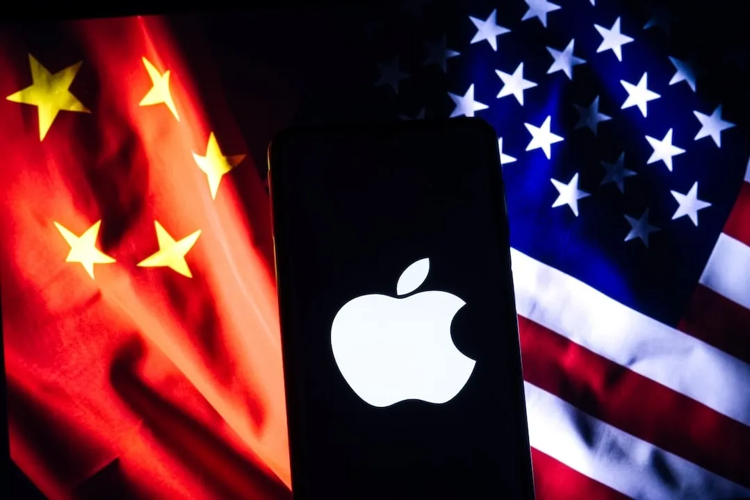 A stark Apple logo on a phone screen with the contrasting flags of China and the U.S. as a backdrop, representing the tech interplay between the two nations.