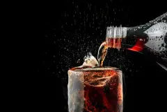 Pour soft drink in glass with ice splash on dark background. 