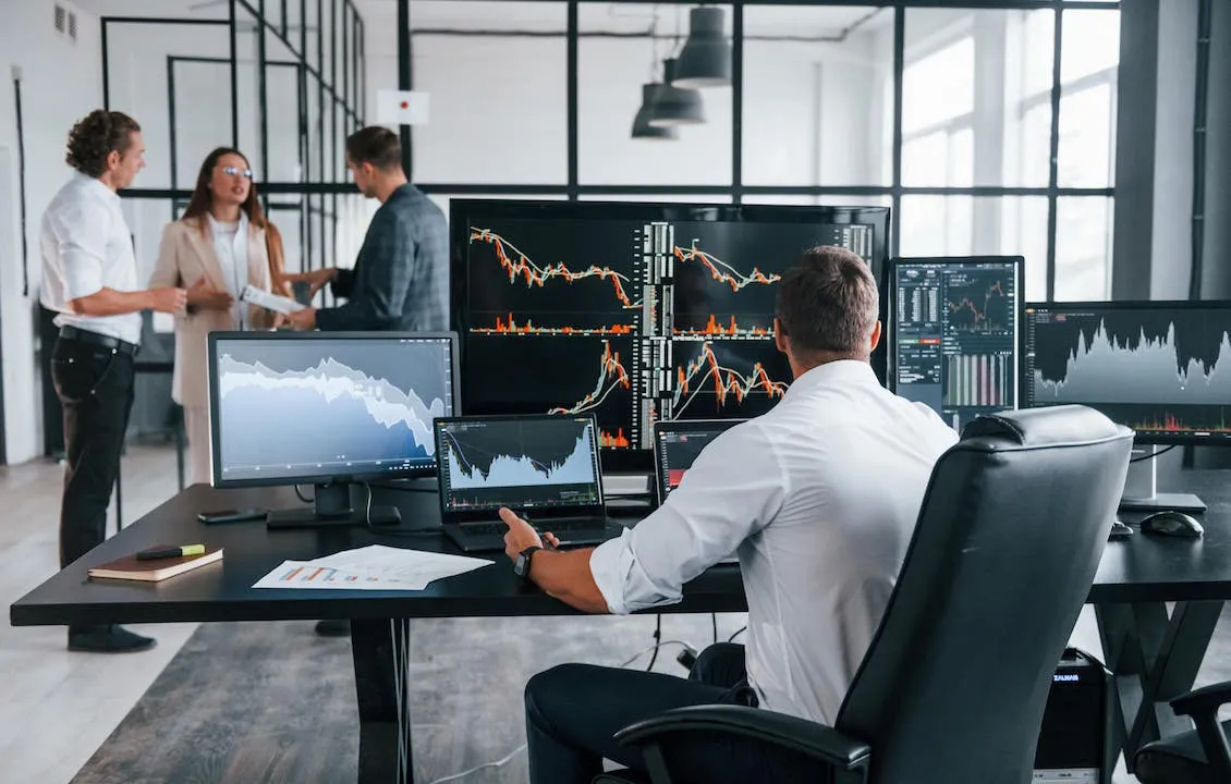 Stock Market Trader monitoring stock charts across multiple monitors on a desk in an office.