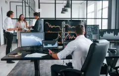 Stock Market Trader monitoring stock charts across multiple monitors on a desk in an office.